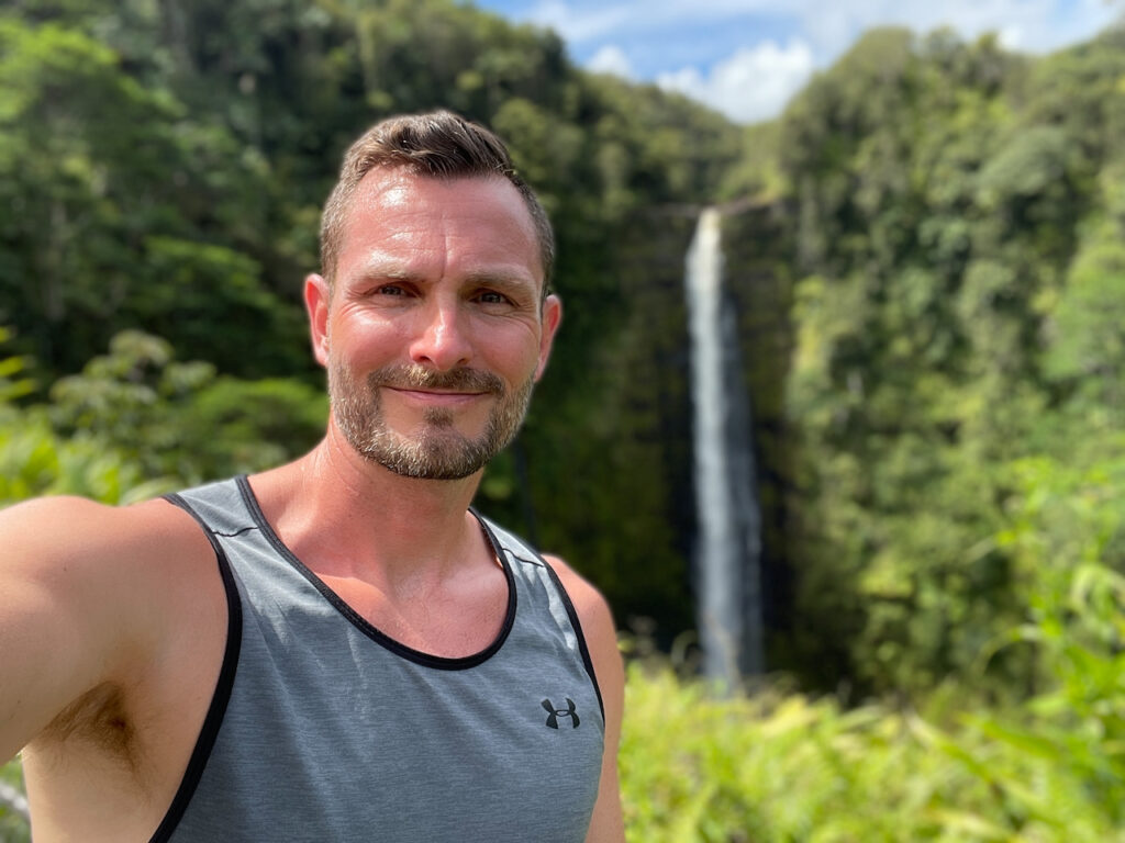 Homo Money smiling in Hawaii with a waterfall behind him
